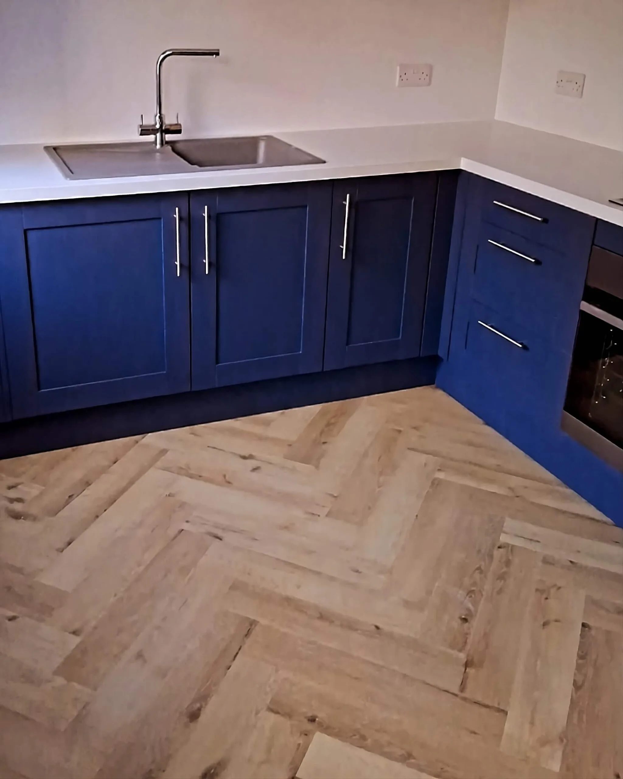 Bespoke blue kitchen installation with herringbone flooring and fitted cabinetry by N. Patten Building & Carpentry, Devon.