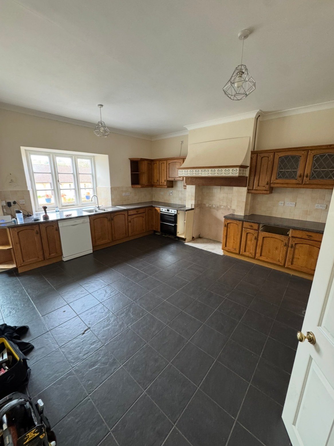 Kitchen before renovation with timber cabinets and dark tiled floor